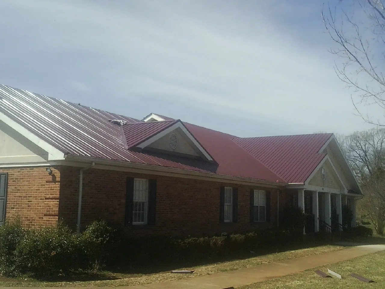 Red metal roof with gabled entries on a long brick building, from a Hail Damage Roof Repair job in Lewistown