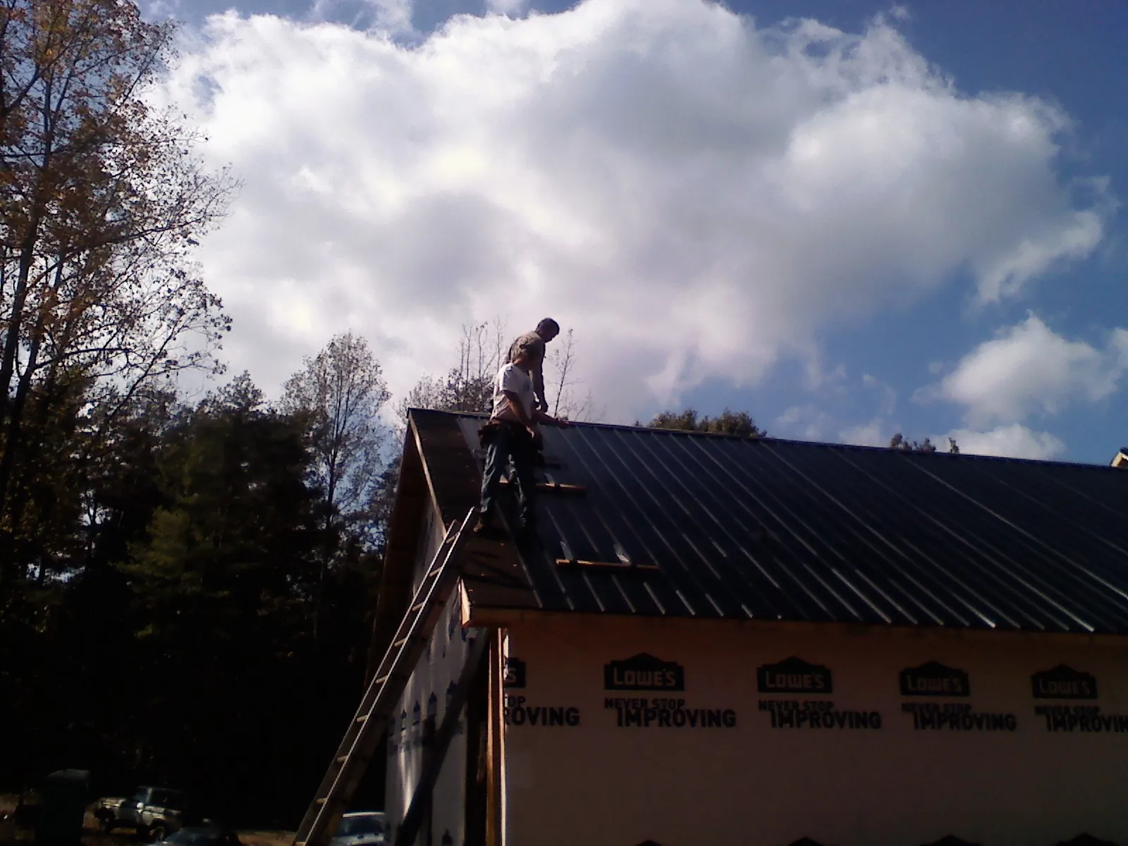 Roofer fastening dark metal panels high against a cloudy sky, from a Roof Inspection job in Lewistown